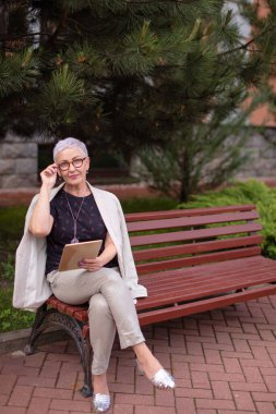 Başarılı, rahat bayan bankta oturuyor ve gözlüğünü tutuyor.