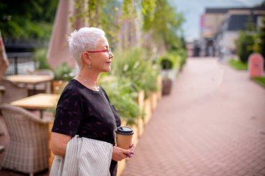 Olgun, mutlu bir turist elinde kahveyle sokakta dikiliyor..