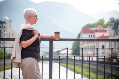 Kadın köprüde dinleniyor ve muhteşem dağlara bakıyor.