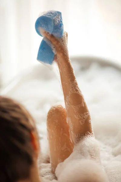 Foto de perto. mulher apertando a esponja no banho com espuma — Fotografia de Stock