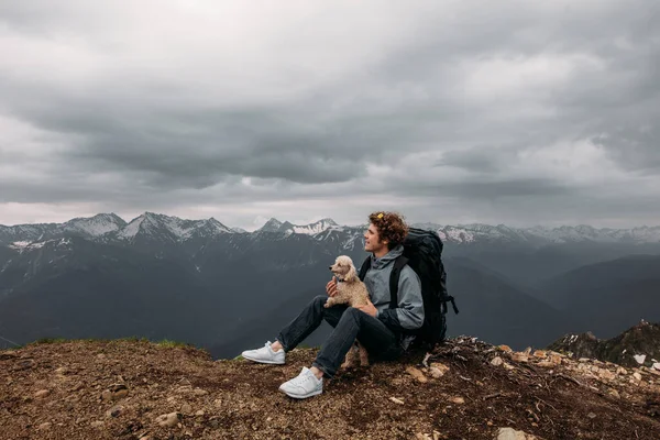 Приємний хлопець з гарною собакою чекає заходу сонця на вершині гори — стокове фото
