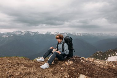 Sırt çantalı genç adam dinlenirken köpeğiyle konuşuyor.
