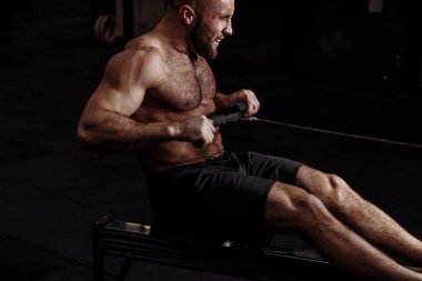 Spor malzemelerinin üzerinde oturan güçlü kaslı bir adam.