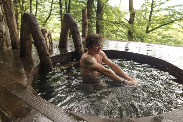 Mann mit lockigem Haar schwimmt nach Saunagang im hölzernen Whirlpool — Stockfoto