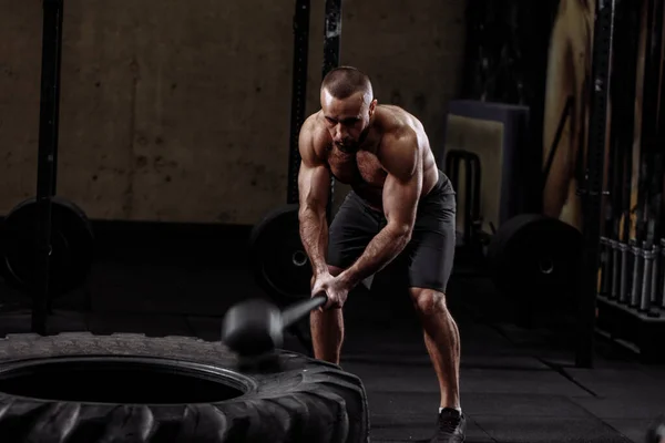 A muscular brutal man is slaming down the tire — Stock Photo, Image