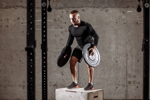 Sportif mâle tient deux plaques de poids et regardant vers le bas — Photo