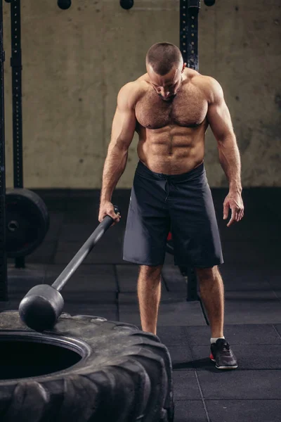 Molesto joven deportista está cansado de hacer ejercicio con martillo y martillo de trineo — Foto de Stock