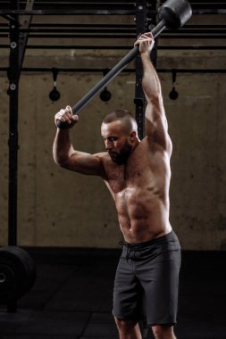 Sportif adam balyozla kol egzersizleri yapıyor.