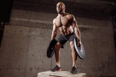 Genç yakışıklı adam halter plakalarıyla çalışmak için vücudunu eğiyor.