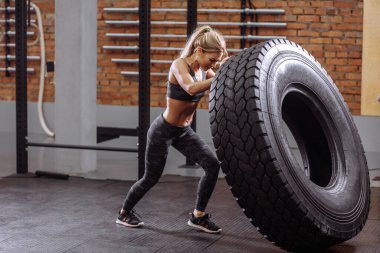 Kadın fitness modeli traktör lastiğiyle spor salonunda antrenman yapıyor..