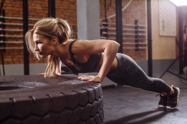 Turp gibi sarışın bir kadın, jimnastik salonunda iç mekanıyla şınav çekiyor.