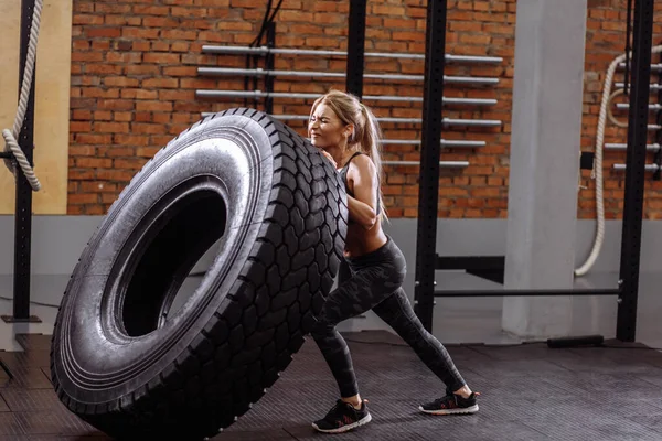 Spor kıyafeti giyen formda bir bayan sporcu büyük bir lastikle çalışıyor. — Stok fotoğraf
