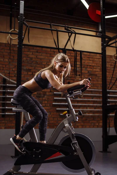 Thoughtful young female is sitting on the exercise bike — Stock Photo, Image