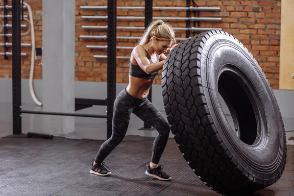 Kadın fitness modeli traktör lastiğiyle spor salonunda antrenman yapıyor.. — Stok fotoğraf