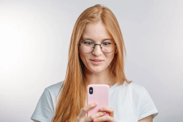 Una chica pelirroja sorprendida está mirando el teléfono — Foto de Stock