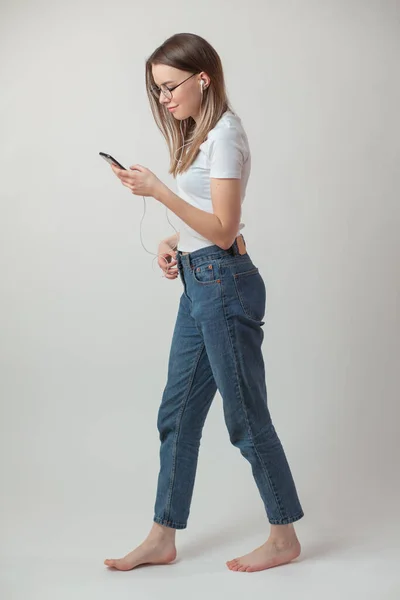 Веселая девушка в повседневной одежде смотрит на смартфон, когда идет куда-то — стоковое фото