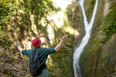 İzlanda 'da şelaleden önce el kaldıran erkek gezginin arka çekimi.
