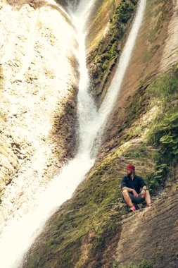 Ormandaki şelalenin yanında sırt çantasıyla kamp yapan genç bir turist..