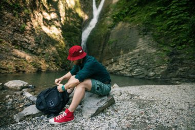 Ormandaki şelalenin yanında sırt çantasıyla kamp yapan genç bir turist..