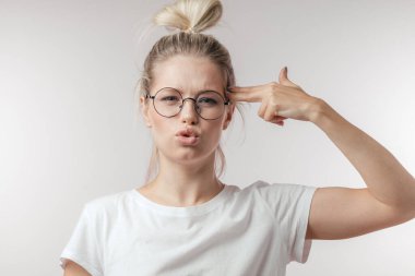 Hoşnut olmayan sarışın kadın tabancayı eliyle taklit ediyor, dudaklarını kıvırıyor, ateş ediyor, izole edilmiş..