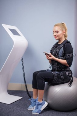 Harika sportif kız topun üzerinde otururken cep telefonuna bakıyor.