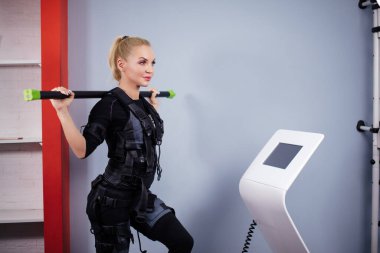 Güzel, sportif kadın, EM cihazındaki sırt kaslarını canlandırmak için çubuk tutuyor.