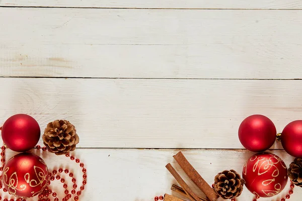 Décoration de Noël avec boules rouges, cannelle, chaîne, cônes sur fond de bois blanc — Photo