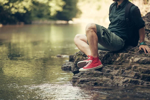 Turista s batohem sedí u jezera v divokém letním lese. Expedice — Stock fotografie