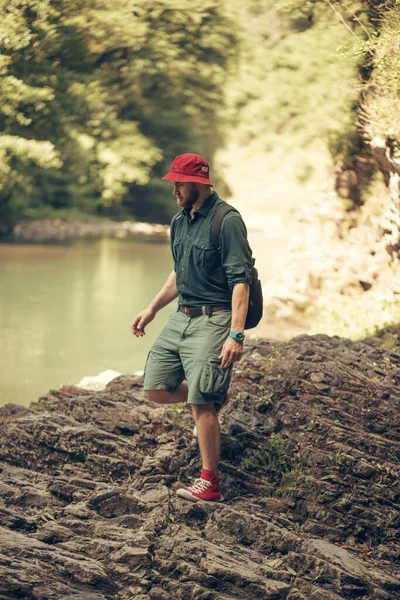 Ragazzo turistico con lo zaino seduto vicino al lago in un bosco selvaggio estate. Spedizione. — Foto Stock