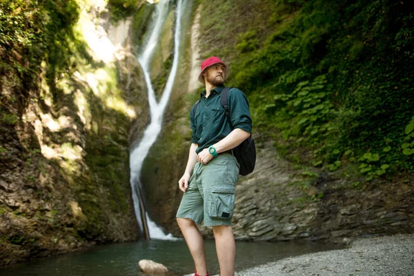 Junger Tourist zeltet mit Rucksack in der Nähe eines Wasserfalls im Wald. — Stockfoto