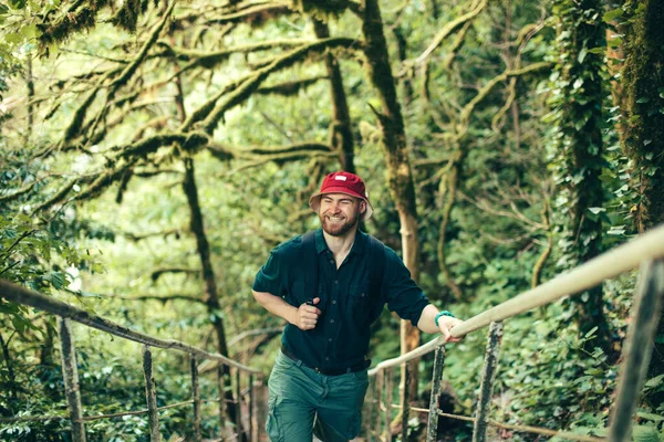 Traveler with backpack climbing over wooden bridge in green forest — Stock Photo, Image