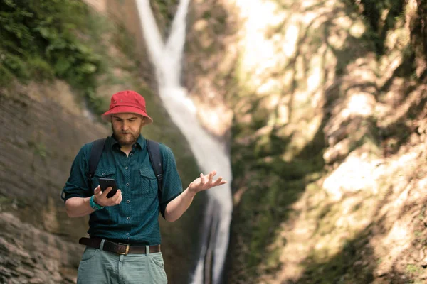 Caminhante detém smartphone tentando encontrar conexão na floresta profunda com cachoeiras. — Fotografia de Stock