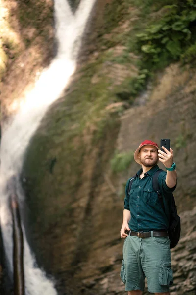 Turysta posiada smartfon próbuje znaleźć połączenie w głębokim lesie z wodospadami. — Zdjęcie stockowe