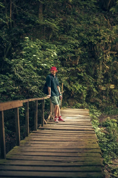 Il viaggiatore attraversa il ponte sospeso nella verde foresta estiva. — Foto Stock