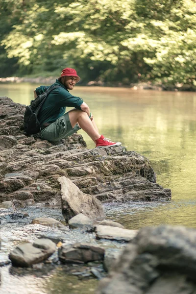 Turista com mochila sentado perto do lago em uma floresta selvagem de verão. Expedição — Fotografia de Stock