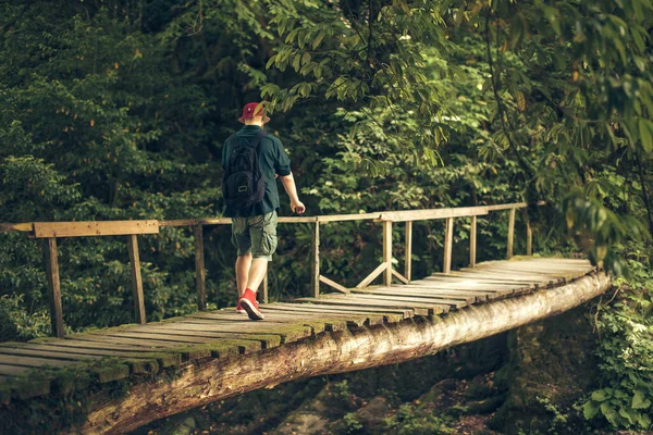 Il viaggiatore attraversa il ponte sospeso nella verde foresta estiva. — Foto Stock