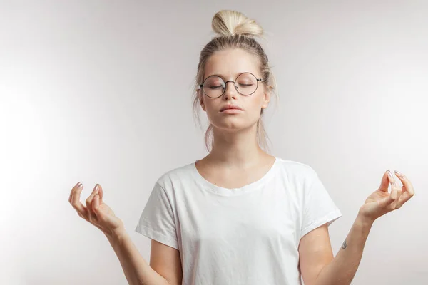 Žena oblečená v bílém tričku se zavřenýma očima při meditaci uvnitř. — Stock fotografie