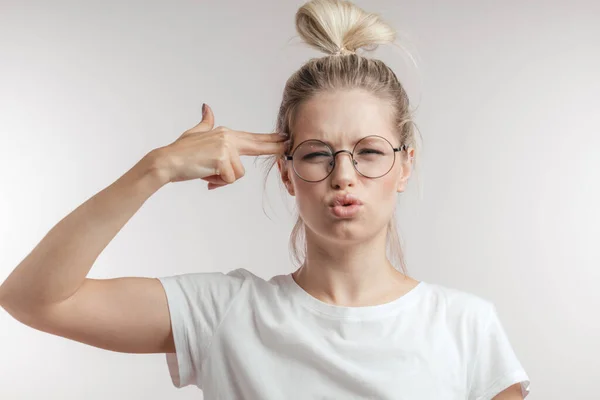 Displeased blonde woman imitates gun with hand, curves lips, shoots, isolated. — Stock Photo, Image