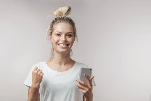 Mujer feliz con el teléfono inteligente en una mano y mirando a la cámara, aislado. — Foto de Stock