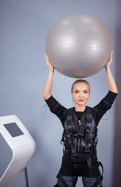 girl wearing electrical muscular stimulation suit doing exercise with ball.