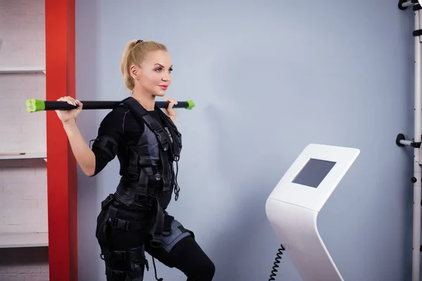 Hermosa mujer deportiva está sosteniendo palo para estimular los músculos de la espalda en el dispositivo ems — Foto de Stock