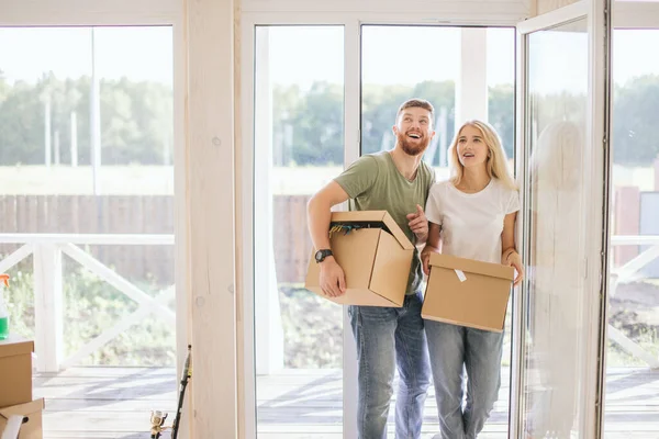 Pareja feliz llevando cajas de cartón en un nuevo hogar en el día de mudanza — Foto de Stock