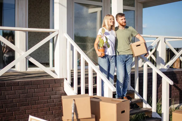 Муж и жена стоят перед новой покупкой дома с коробками — стоковое фото