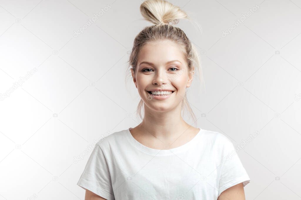 Happy smiling woman with blonde hair bun poses alone against white background.