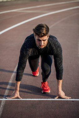 Sporcu koşu pistinde başlangıç pozisyonunda. Stadyum pistinde koşu antrenmanı yapan koşucu