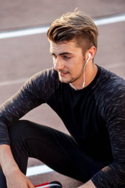 Stadyumda oturmuş kulaklıkla müzik dinleyen bir adam.