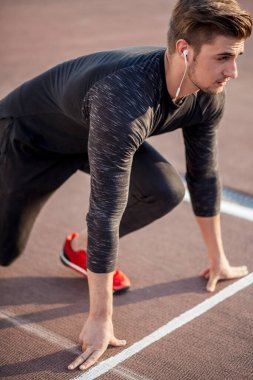 Sporcu koşu pistinde başlangıç pozisyonunda. Stadyum pistinde koşu antrenmanı yapan koşucu