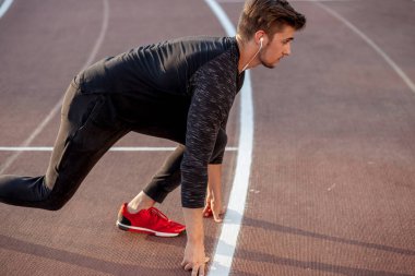 Sporcu koşu pistinde başlangıç pozisyonunda. Stadyum pistinde koşu antrenmanı yapan koşucu