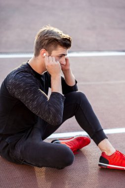 Stadyumda oturmuş kulaklıkla müzik dinleyen bir adam.