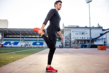 Adam stadyumdaki yarış pistinde koşmadan önce vücudu gerer.